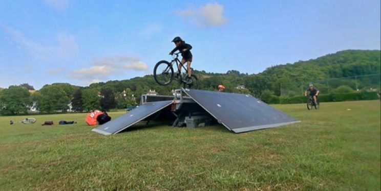 A young person on a bike wearing a full helmet jumps over a ramp.