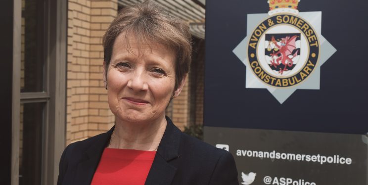 Clare Moody standing in front of the Avon and Somerset Police logo outside the police headquarters, smiling and looking to camera