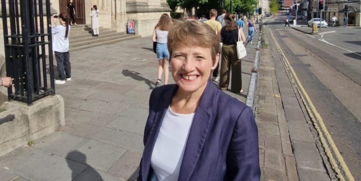 PCC Clare Moody is stood on a Bristol street, wearing a blue suit, smiling