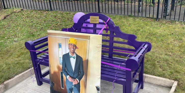 An image of a LARGE photo of Eddie against a new purple remembrance bench in a park