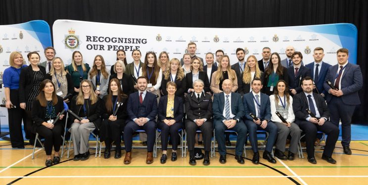 An image of approx 40 people stood up and sat down in rows, smiling to camera and holding certificates. PCC Clare Moody is sitting in the middle centre next to CC Sarah Crew